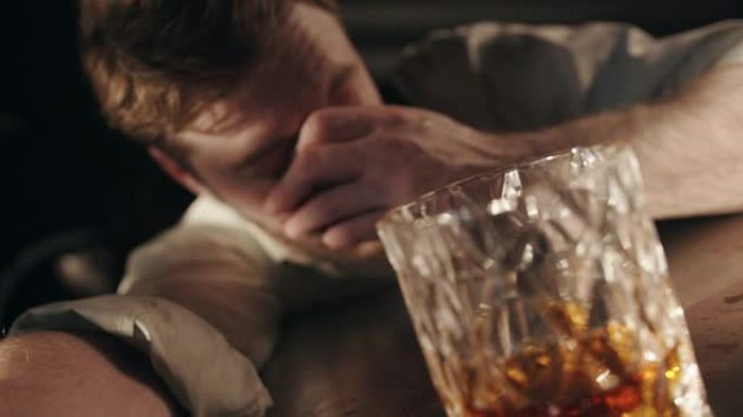 一个在酒吧里睡着的醉汉醒来，从一杯威士忌中喝了一口
