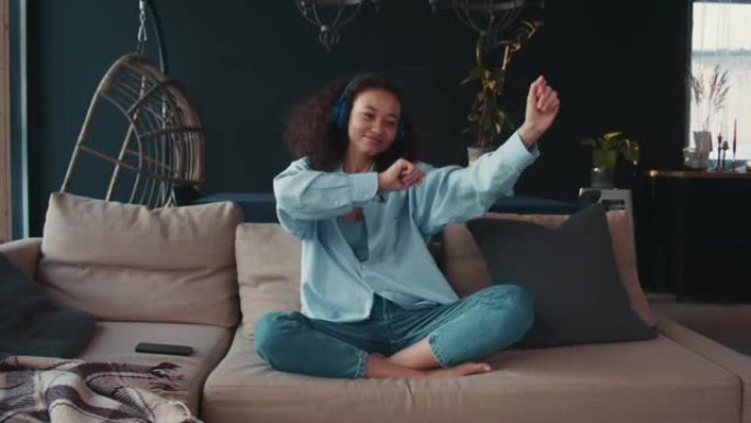 顶视图快乐积极放松美丽的年轻非洲裔美国妇女在家里用无线耳机随着音乐跳舞。