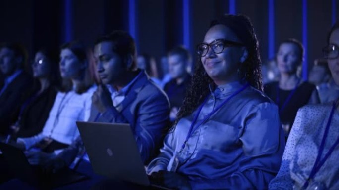 在国际商务会议上，黑人女性坐在黑暗拥挤的礼堂里。多种族的非洲妇女使用笔记本电脑。代表观看有关新财务解