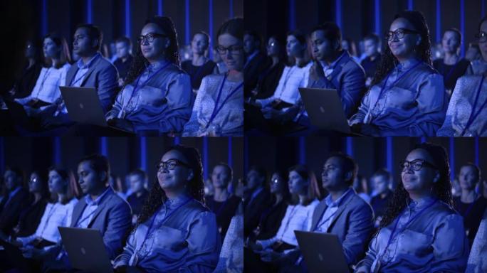 在国际商务会议上，黑人女性坐在黑暗拥挤的礼堂里。多种族的非洲妇女使用笔记本电脑。代表观看有关新财务解