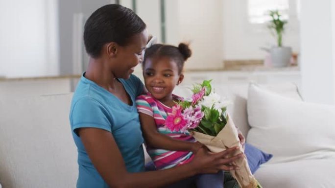 快乐的非洲裔美国母女坐在沙发上闻着鲜花
