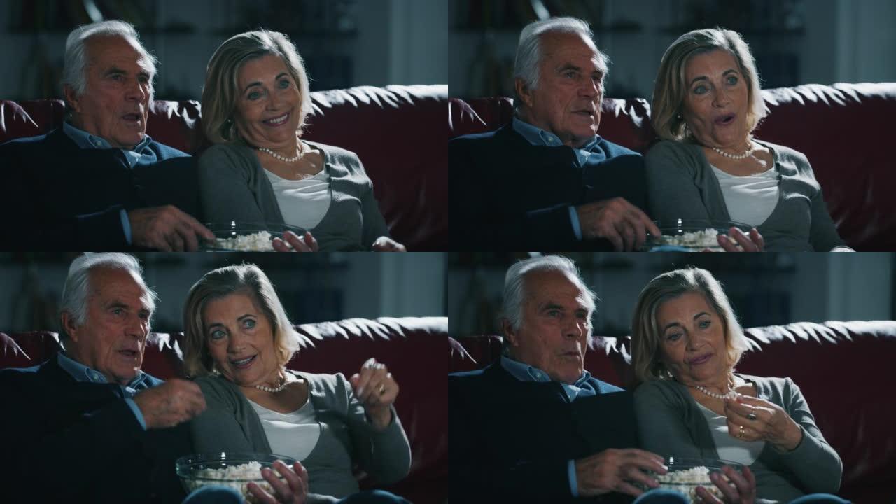 一对幸福的高级夫妇的特写镜头是喜欢在电视上看电影，在家里的客厅的沙发上吃爆米花。