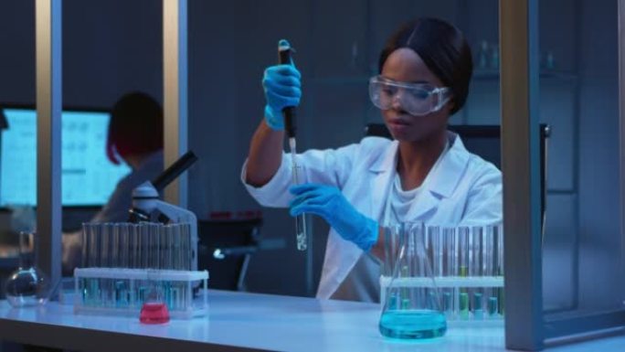 一位年轻的非裔美国女化学家在带有玻璃试管的现代实验室中工作，戴着防护眼镜