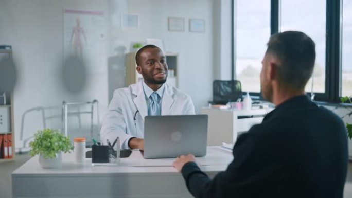家庭医生在健康诊所咨询期间提供有关男性患者医疗结果的好消息。穿着白大褂的医生坐在医院办公室的电脑后面