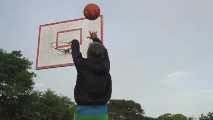 一名亚洲华裔资深男子早上在篮球场练习篮球赛跳投