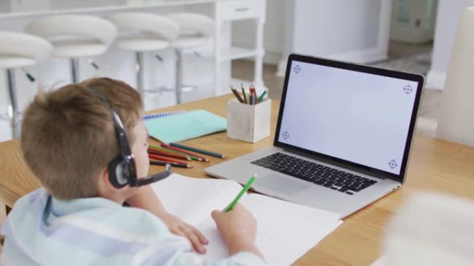 快乐的高加索男孩在网上学校课程中使用耳机和笔记本电脑，在屏幕上复制空间
