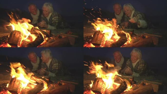 资深夫妇坐在冬季海滩上着火