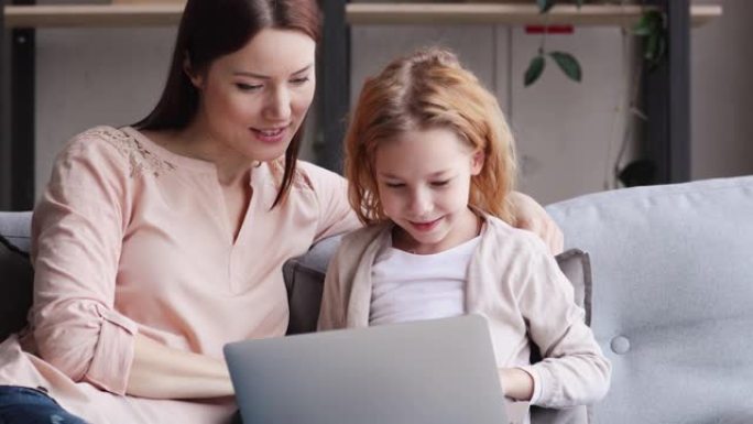 有爱心的年轻妈妈在电脑上向女儿展示教育应用。