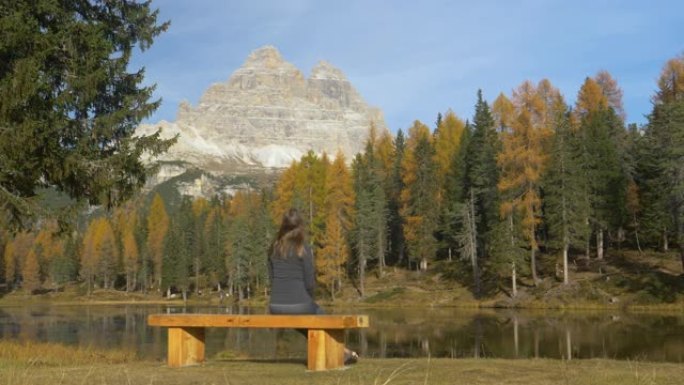 复制太空女人坐在长凳上观察秋天的山湖景观