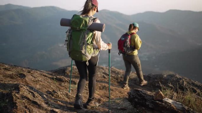 两个女人徒步上山，在山顶上击掌，举手庆祝成功