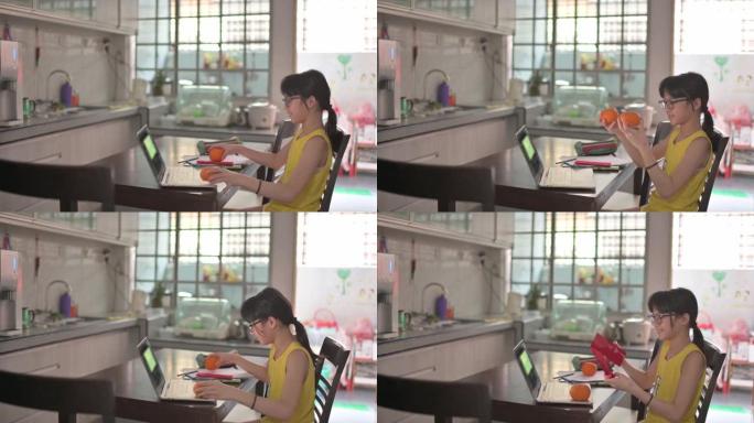 亚洲华裔年轻女孩看着笔记本电脑摄像头，用红色信封和橘子向祖父母问候农历新年庆祝活动