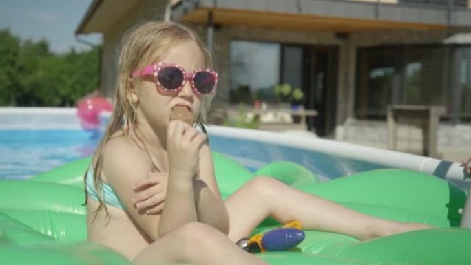 关闭可爱的女孩漂浮在游泳池里，在炎热的夏日吃冰淇淋