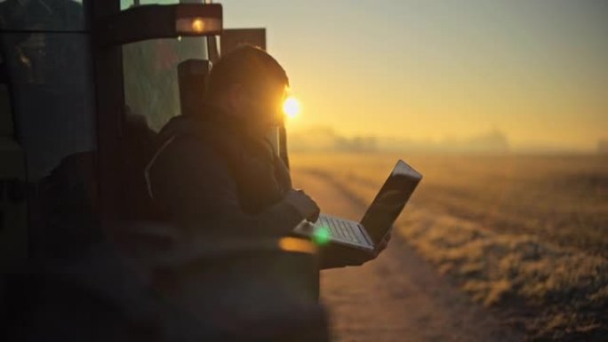 日出时在农村地区用拖拉机在笔记本电脑上工作的男性农民