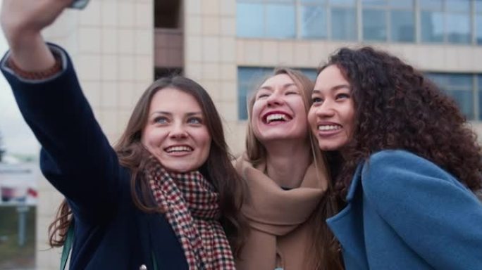 快乐兴奋的美丽的年轻多民族女性使用智能手机摆姿势拍照，在秋日外面微笑。