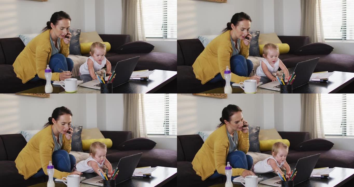 白人母亲在家工作时抱着婴儿做笔记并在智能手机上聊天
