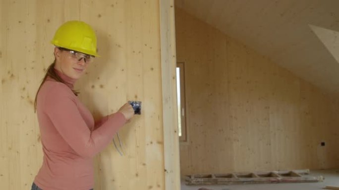 肖像: 年轻的女电工将出口框架拧到木墙上