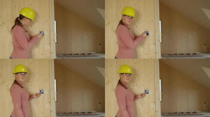 肖像: 年轻的女电工将出口框架拧到木墙上