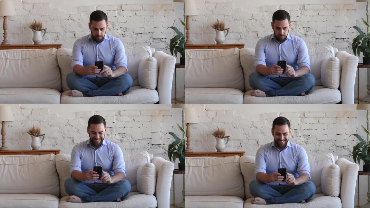微笑的英俊单身男人在家沙发上使用智能手机