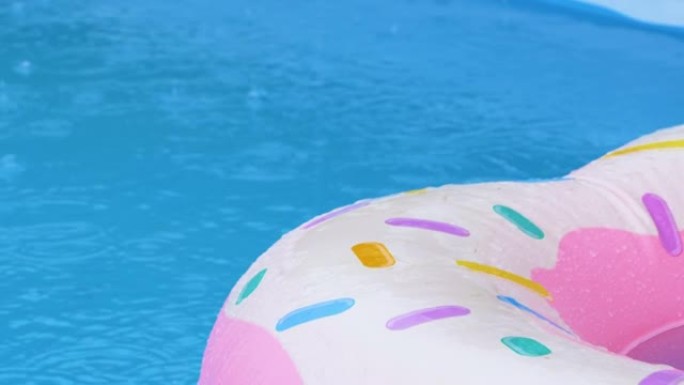 特写: 雨水开始倾泻在漂浮在游泳池周围的充气甜甜圈上。