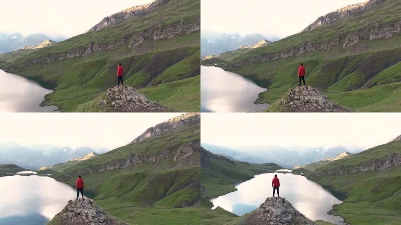 空中拍摄的男子徒步旅行者爬到山顶，举起双臂向天空拍摄全景山日出