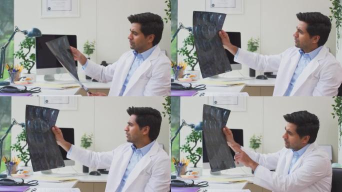 男性医生或全科医生穿着白大褂坐在办公室的办公桌上查看CT或MRI扫描-慢动作拍摄