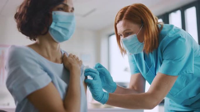 戴着安全手套和防护口罩的医护人员正在健康诊所为女性患者注射疫苗。医生使用皮下注射针和注射器注射药物作