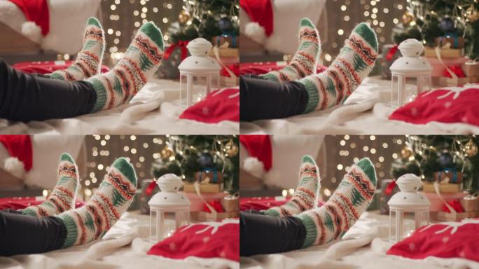 一个穿着圣诞节图案的袜子的男人坐在圣诞树附近的毯子上，移动双腿