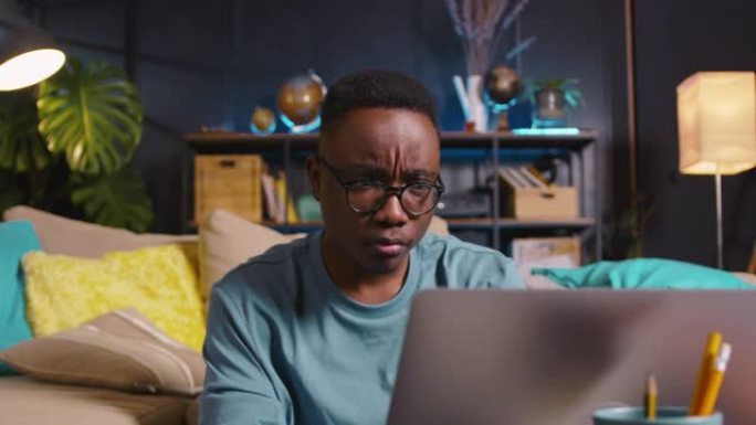 年轻快乐的gen-z黑人男生戴眼镜，用笔记本电脑在舒适的家中在线学习表达各种情感。