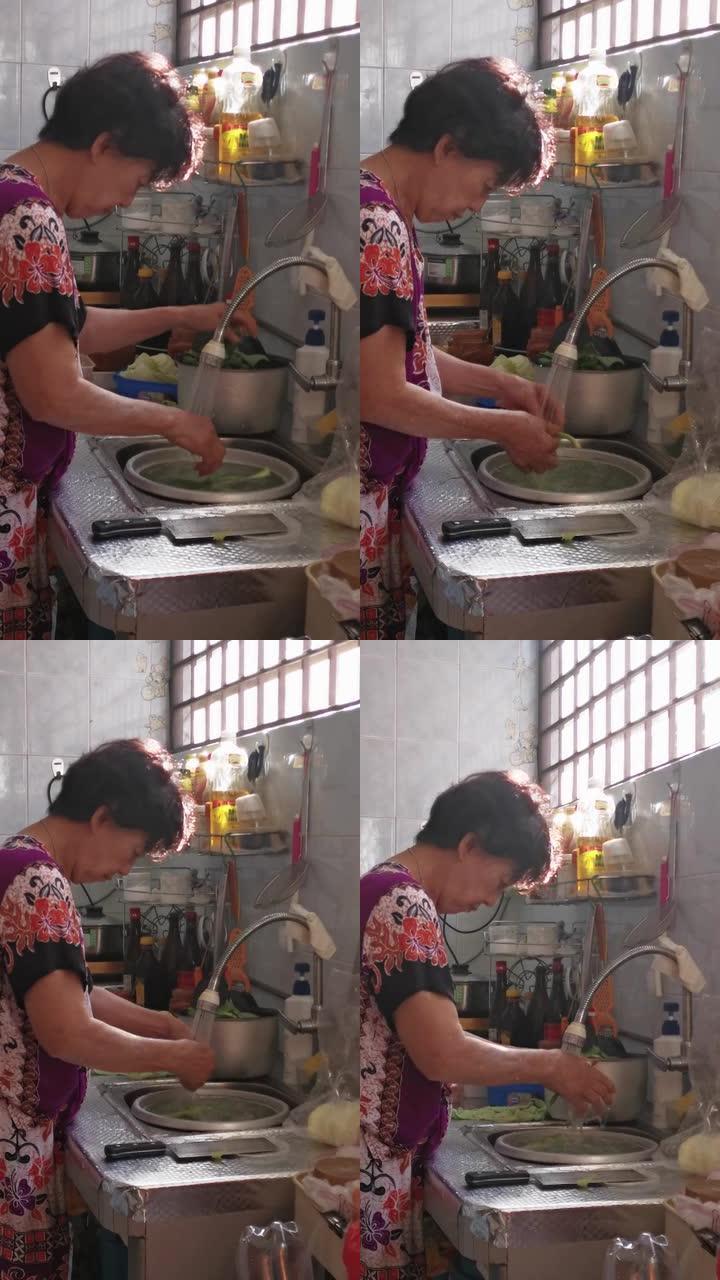 亚洲华裔高级妇女在厨房做饭，在水槽里洗菜