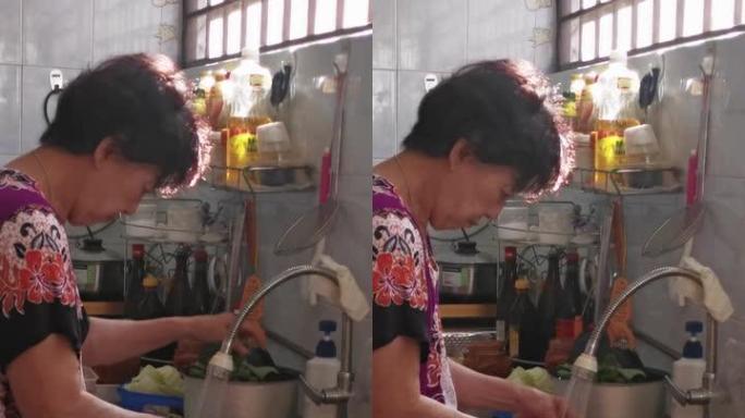 亚洲华裔高级妇女在厨房做饭，在水槽里洗菜