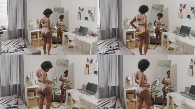 弯曲的黑人妇女在镜子前测量她的腰部