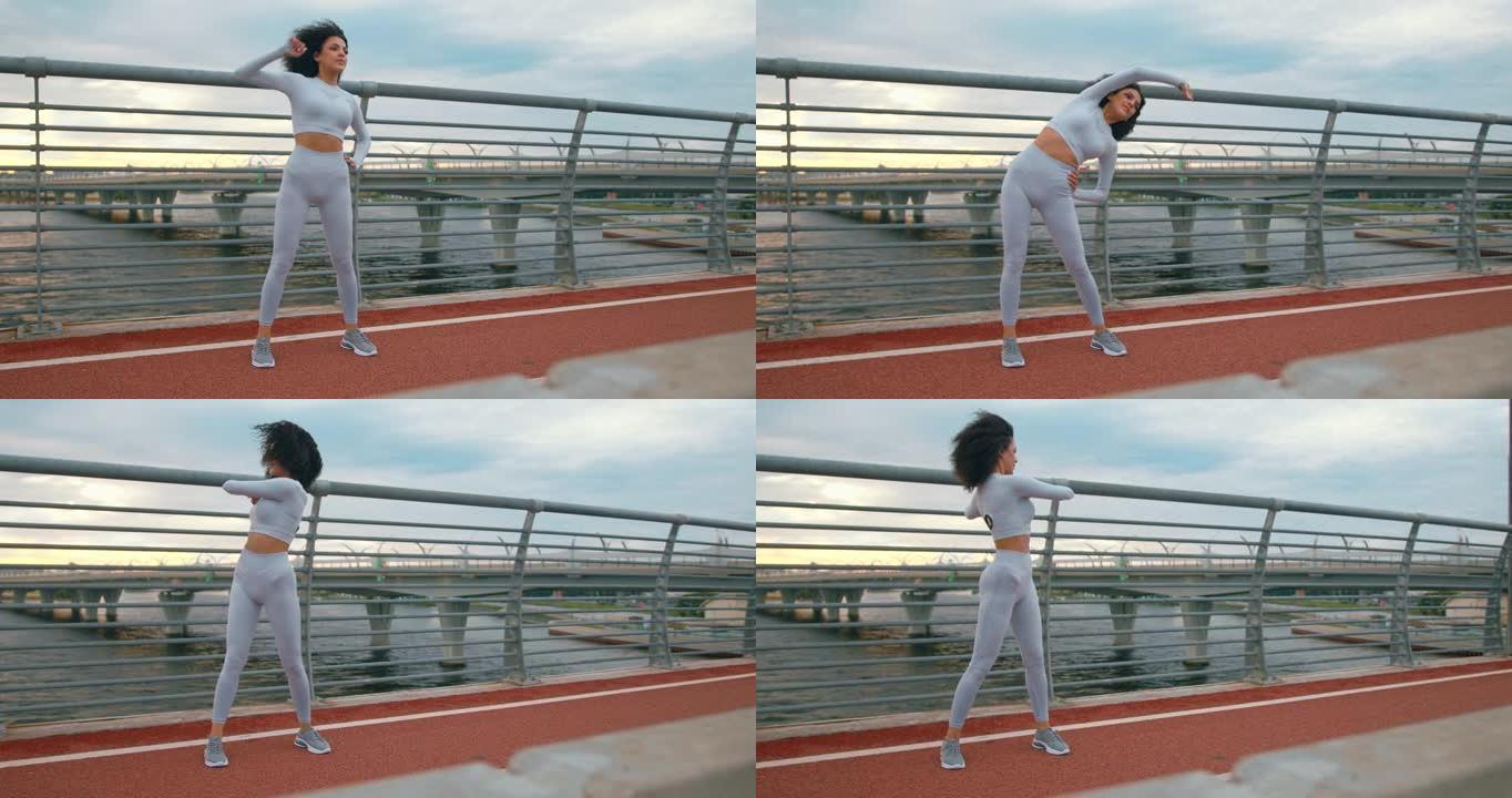 一位年轻健康的女跑步者穿着白色运动服，卷发，正在桥上热身。