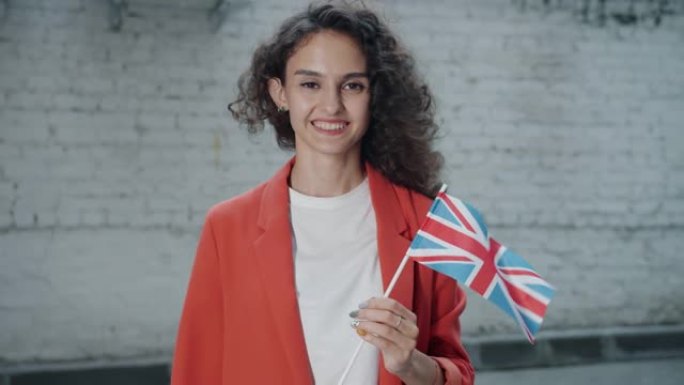 在多风的夏日，举着英国国旗的迷人女孩在户外微笑着看着相机的慢动作