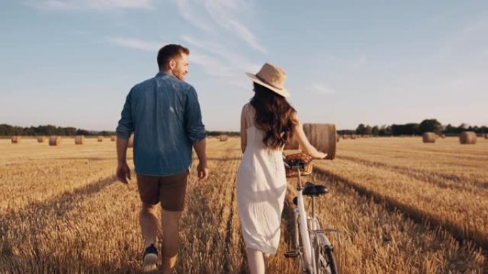 追踪，慢动作镜头的一对成年夫妇牵着手走在收获的田地上，在阳光明媚的日子里骑自行车