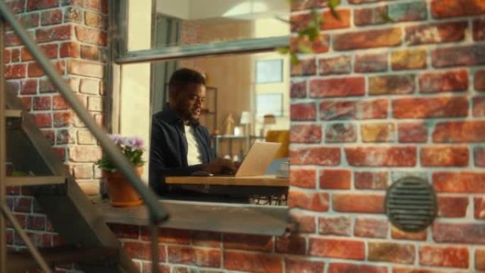 年轻的非洲学生在家里使用笔记本电脑。白天参加在线课程。英俊的男人坐在桌子旁，在计算机上工作，集思广益