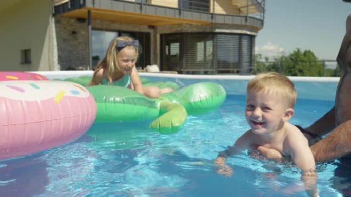 特写: 年轻的家庭在后院游泳池里玩耍，而小男孩试图游泳
