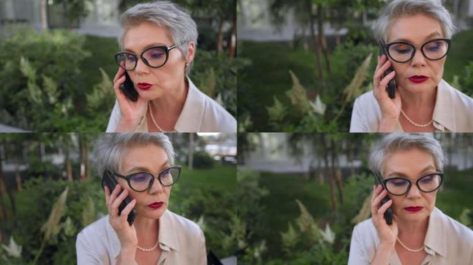 一位头发花白的美丽商务女士的特写镜头，发型时尚，戴着眼镜，正在认真地在电话上聊天，