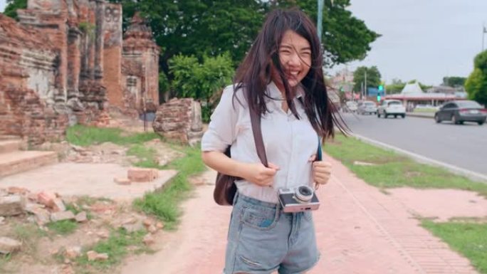 年轻快乐的亚洲背包客博客女游客拿着相机走路，带着快乐的微笑奔跑，在老城街上兴奋地旅行。