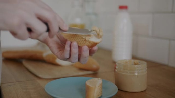 男人在厨房里煮三明治时，用刀在面包上撒上花生酱的手的特写镜头