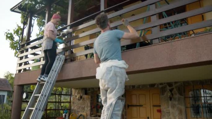 SLO MO夫妇用梯子粉刷房子上的木栅栏