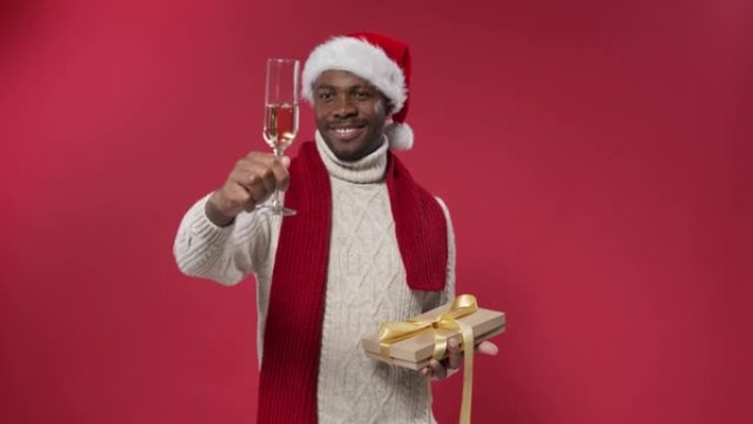 一个戴着圣诞帽和羊毛针织毛衣的黑皮肤男人微笑着拿着一杯香槟和一个礼品盒