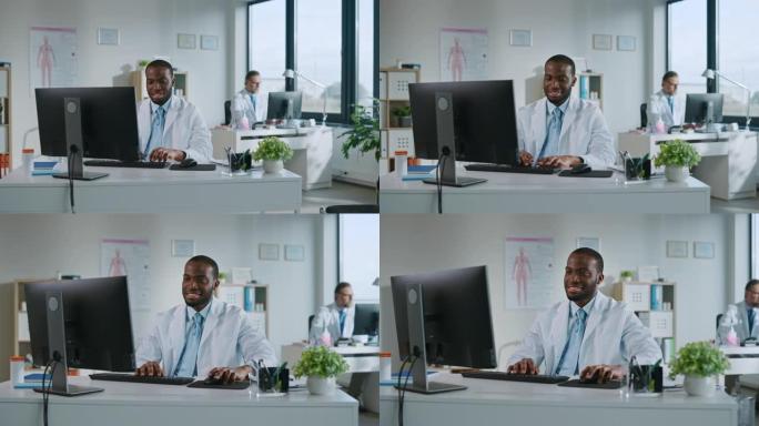 快乐微笑的非洲裔美国医生正在一家诊所的电脑上工作。穿着白大褂的医生正在医院办公室的桌子后面浏览病史。