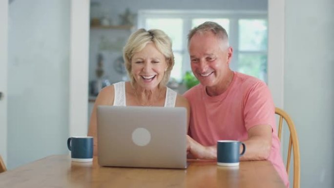 退休夫妇在厨房的家中使用笔记本电脑与家人进行视频通话