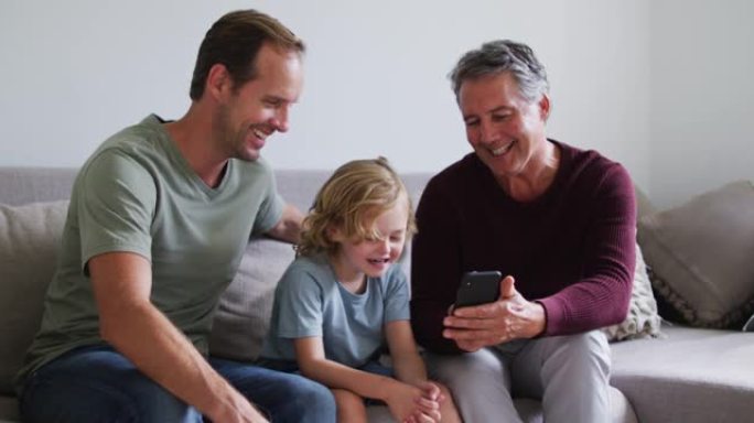 高加索人的祖父，父亲和儿子在家里一起使用智能手机时微笑着