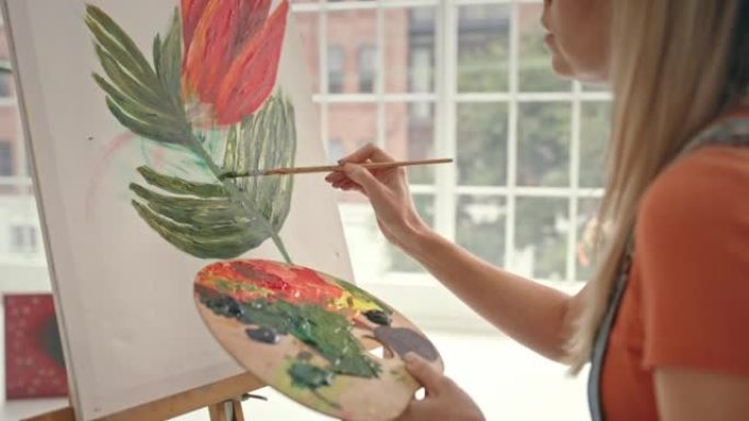 有创造力的女艺术家使用调色板和画笔在画布上绘画。艺术家在她的工作室里发展了她的绘画技巧。年轻女子在艺