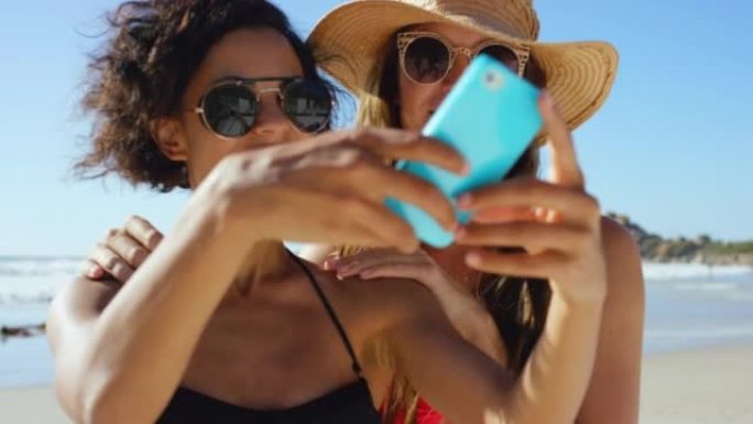 两个迷人的年轻朋友一起站在海滩上并在手机上自拍的4k视频片段