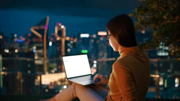 女人坐在屋顶露台上，晚上使用笔记本电脑