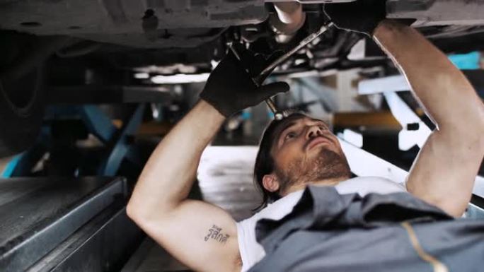 英俊的机械师在汽车服务中使用棘轮在汽车下方工作