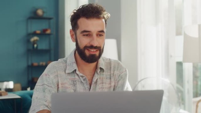 英俊的成年男子，卷曲的黑发使用笔记本电脑，坐在公寓的客厅。集中的人在家工作，网上购物，看视频或写电子
