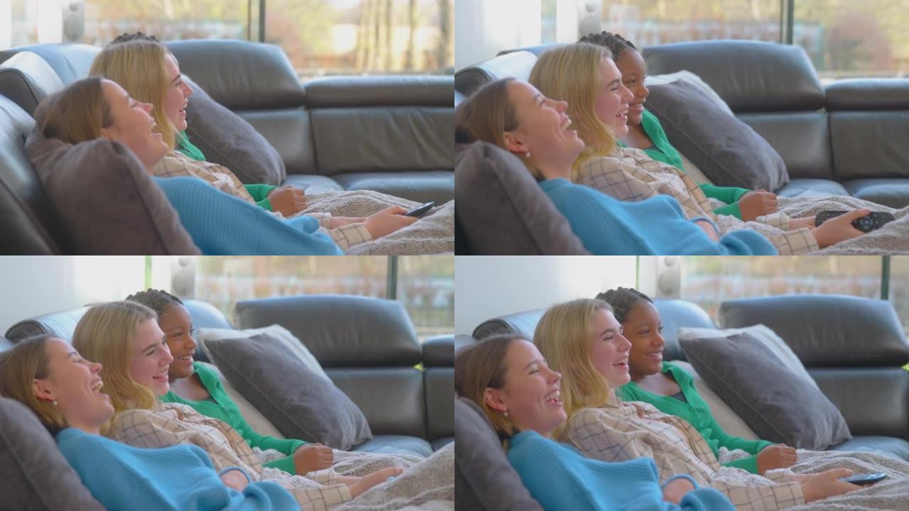 一群多元文化的少女朋友坐在沙发上依偎在家里的毯子下一起看电视 -- 慢动作拍摄